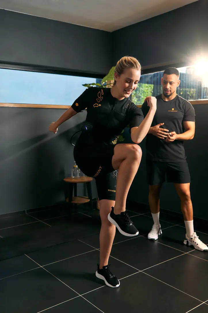 Découvrez l’entraînement SYMBIONT EMS dans votre studio EMS local. Un coach personnel guide un client en combinaison SYMBIONT EMS lors d’une séance d’essai dans un studio EMS local. Vivez un entraînement personnalisé, un accompagnement sur mesure et une motivation optimale pendant votre séance d’essai EMS.