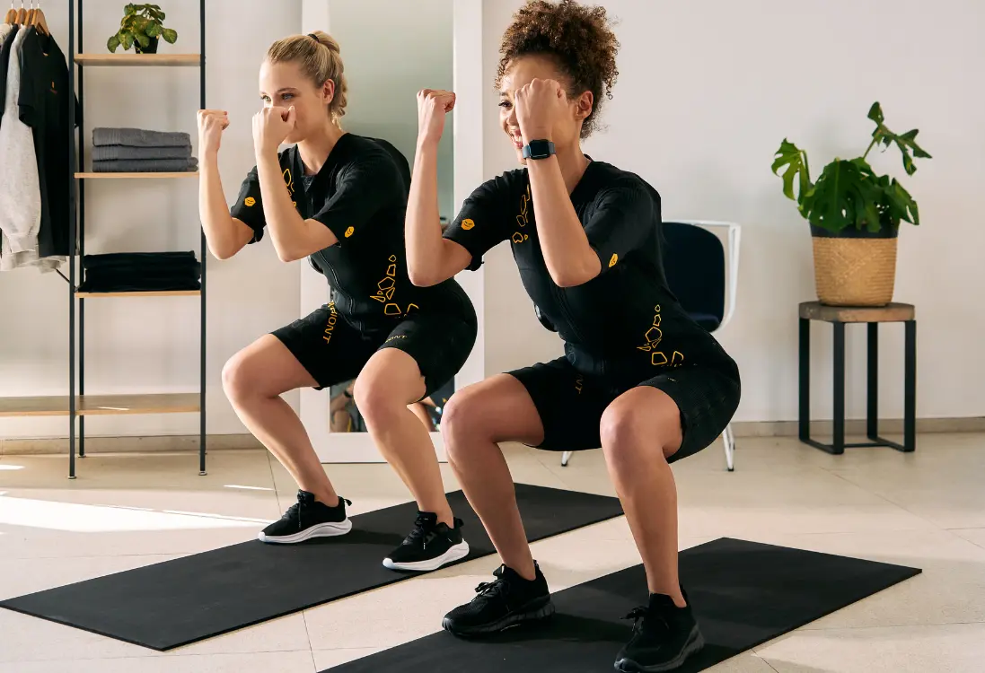 Des résultats rapides avec l'entraînement EMS à Strasbourg Deux femmes en combinaisons EMS réalisent des squats pour des résultats visibles en un temps record.