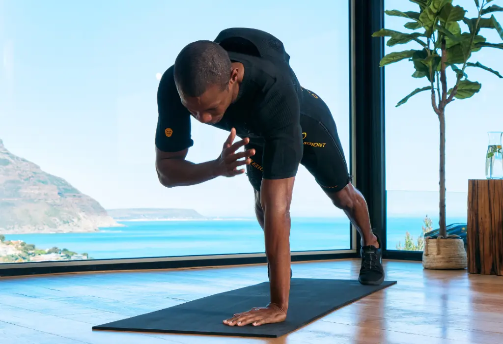 Atteindre ses objectifs avec l'entraînement EMS à Versailles Un homme en combinaison EMS effectue l'exercice de la planche et utilise l'entraînement EMS à Versailles pour atteindre ses objectifs de remise en forme.